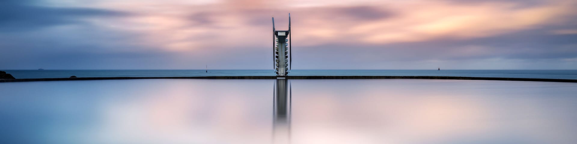 A calm sea with a pier extending into it, under a twilight sky.