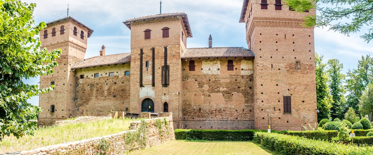 A historic brick castle with multiple towers and a well-maintained garden.