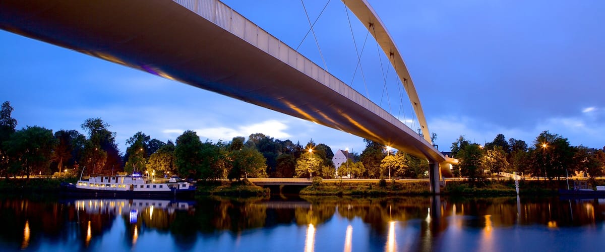 A bridge over a calm river at dusk with a boat docked on the left.