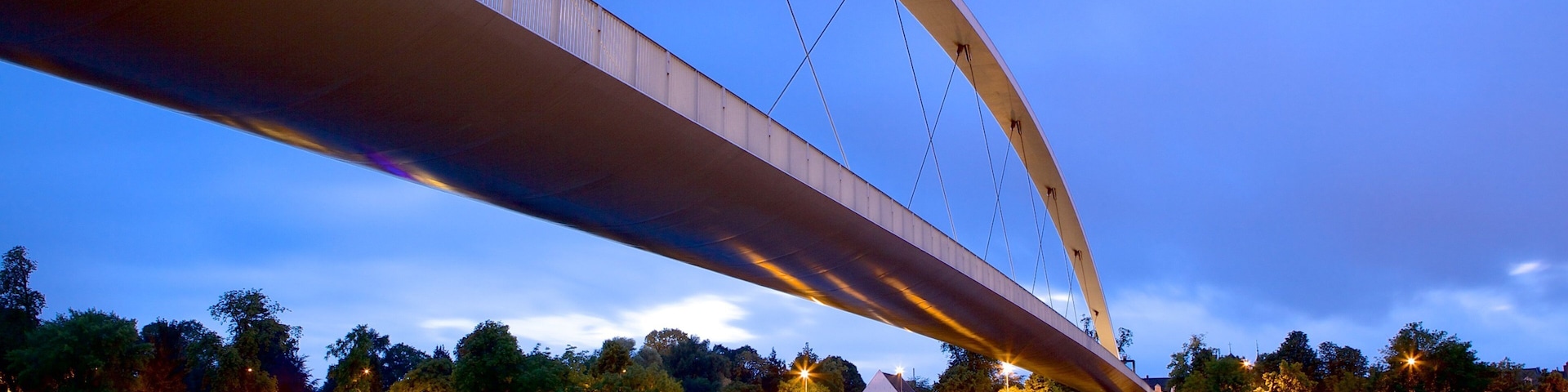 A bridge over a calm river at dusk with a boat docked on the left.