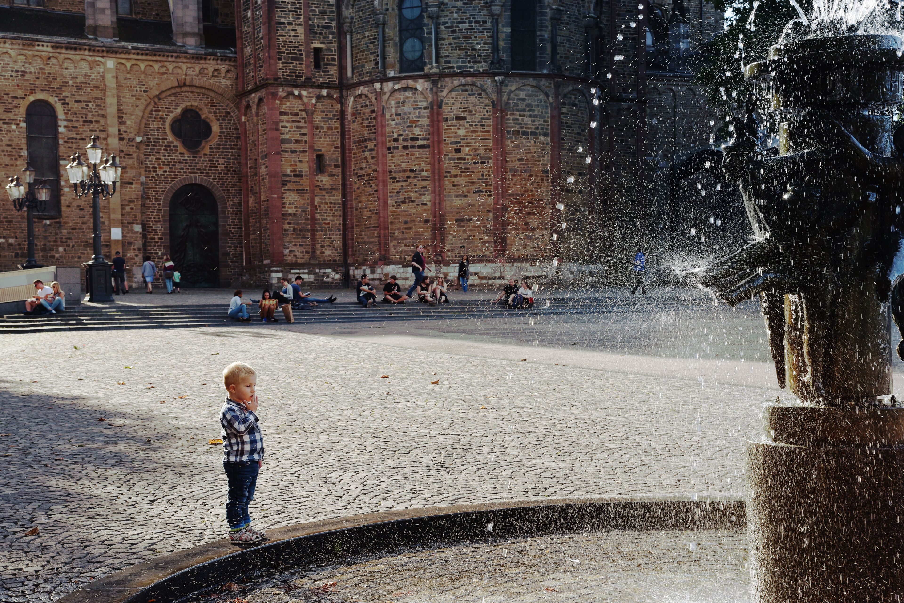 Una plaza adoquinada con una fuente, edificios históricos de ladrillo y un niño junto al agua.