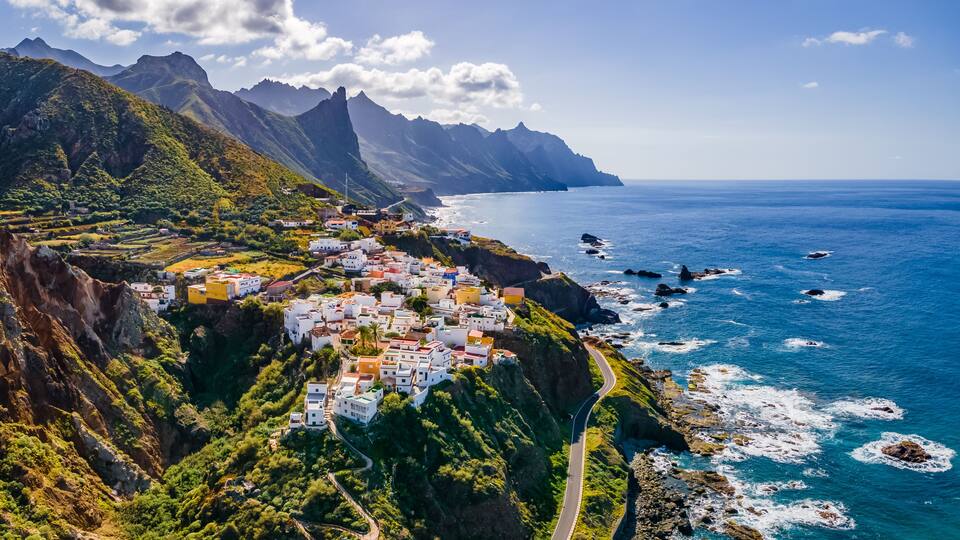 A coastal village with white houses, a winding road, and a rugged coastline.