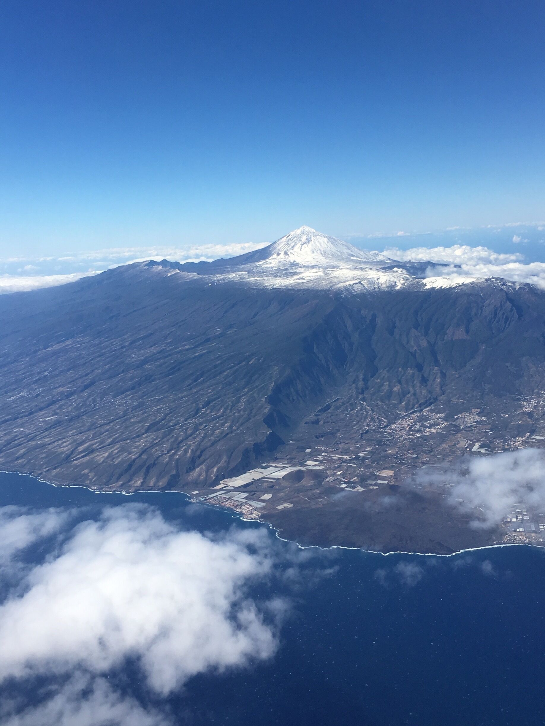 A snow-capped mountain with a clear sky above and a coastline below.