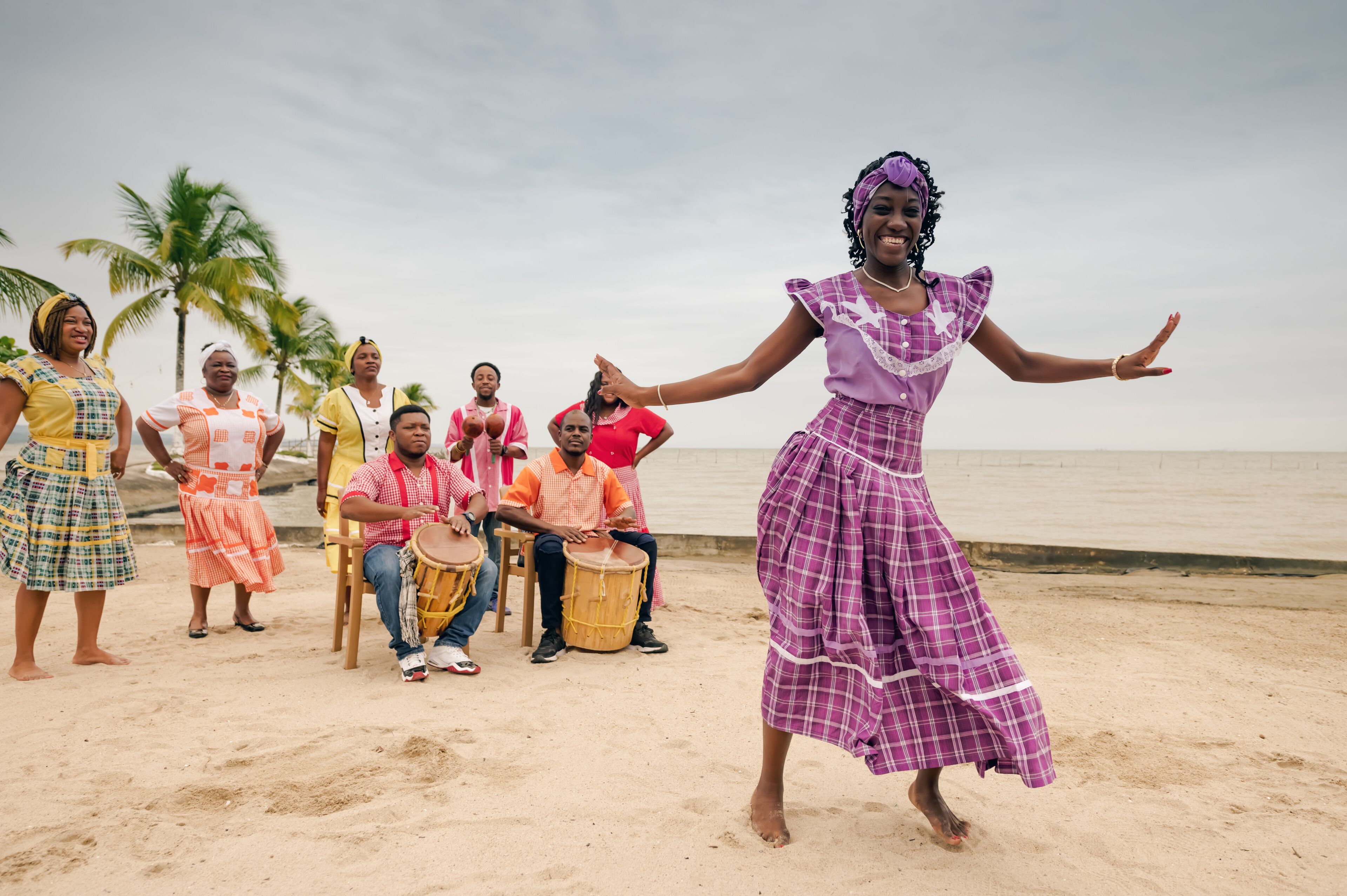 Beautiful black woman dances on a Caribbean beach during a party, wearing a lilac dress.