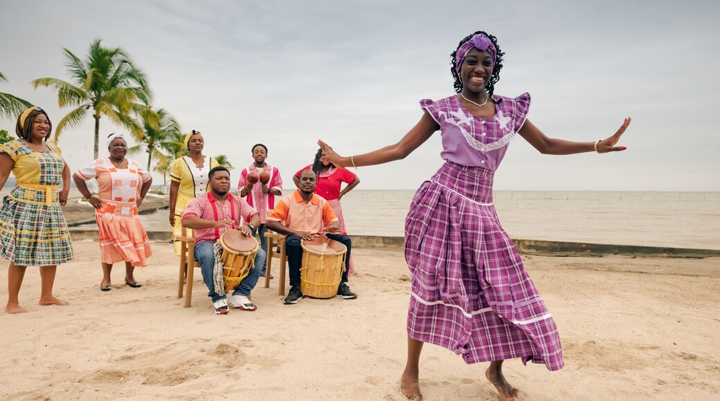 Beautiful black woman dances on a Caribbean beach during a party, wearing a lilac dress.