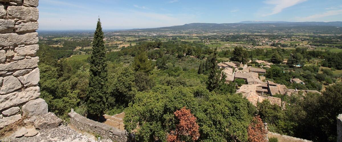 A stone wall overlooking a village with trees and distant hills.
