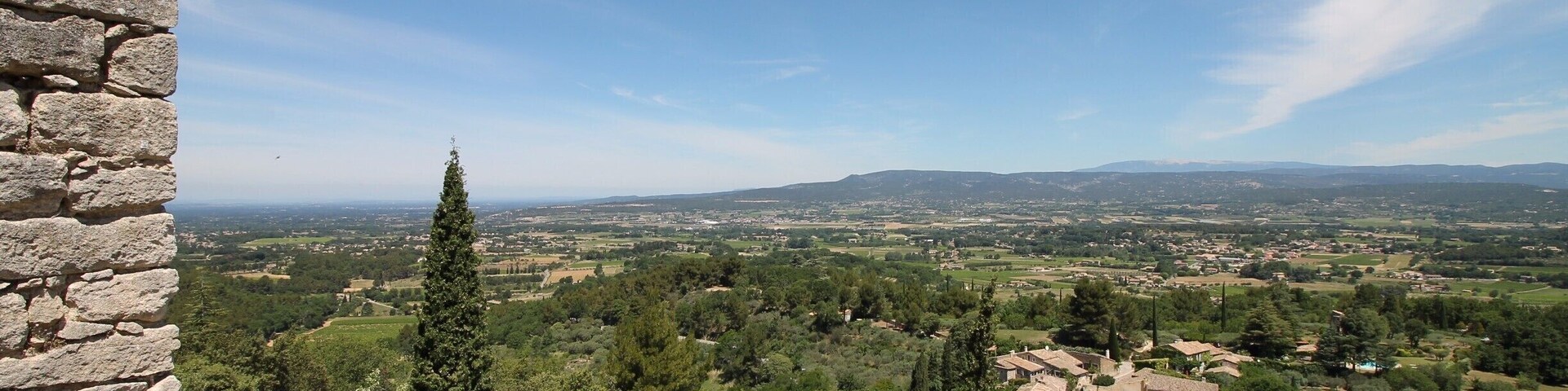A stone wall overlooking a village with trees and distant hills.