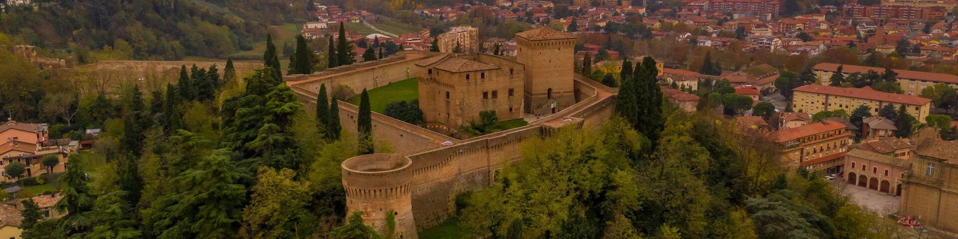 A historic castle surrounded by lush greenery, overlooking a cityscape with rolling hills in the background.