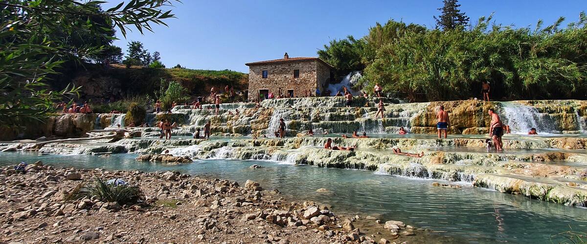 A natural hot spring area with multiple cascading water terraces and a stone building in the background.
