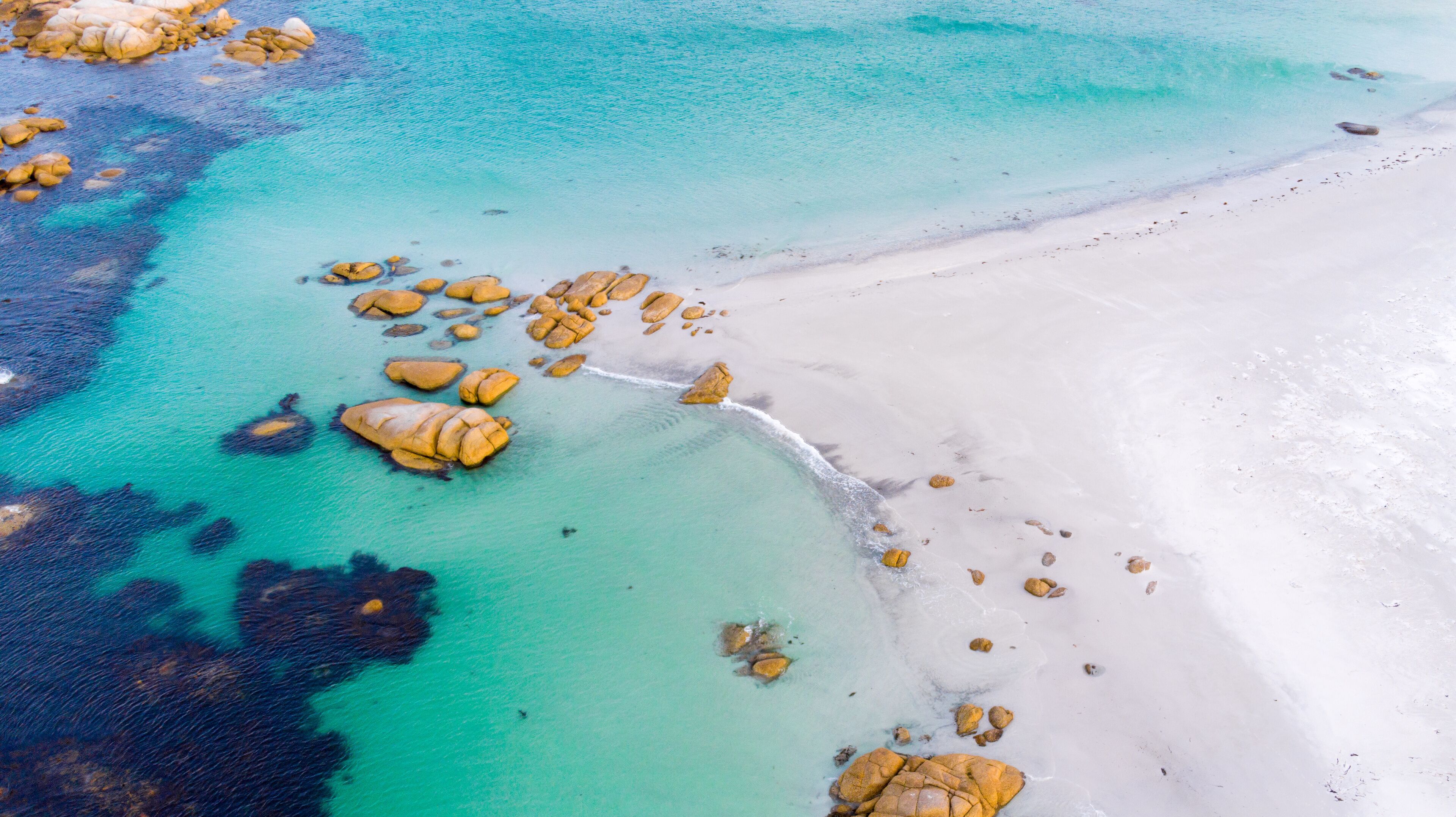 A turquoise sea with white sandy beach and scattered rocks.