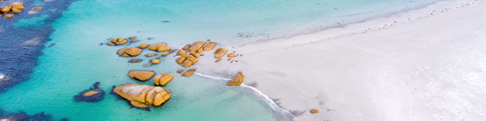 A turquoise sea with white sandy beach and scattered rocks.
