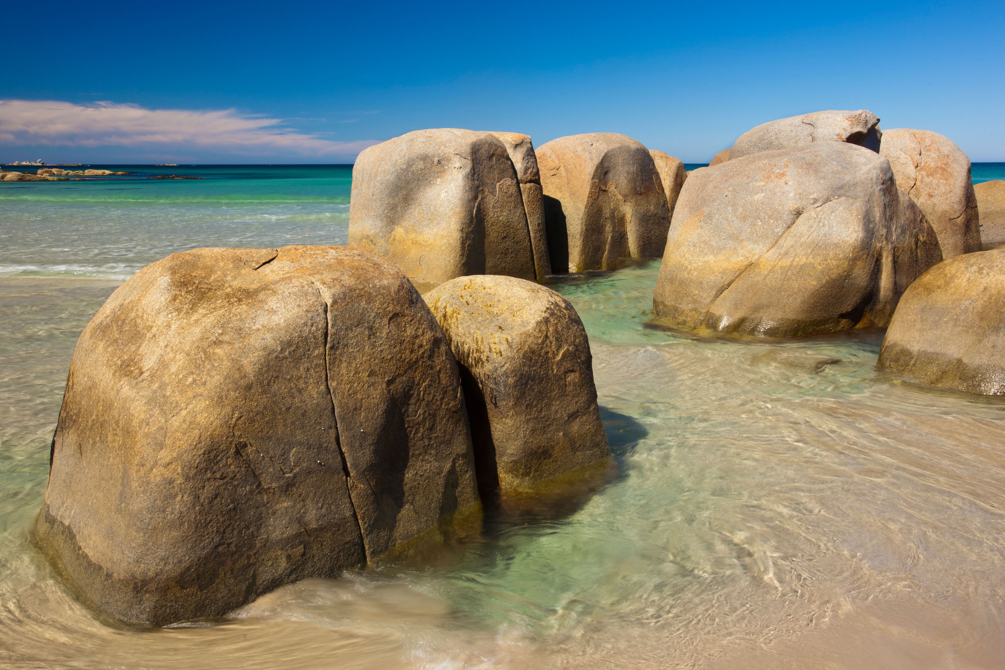 Large boulders in shallow water with clear turquoise sea and a clear blue sky.