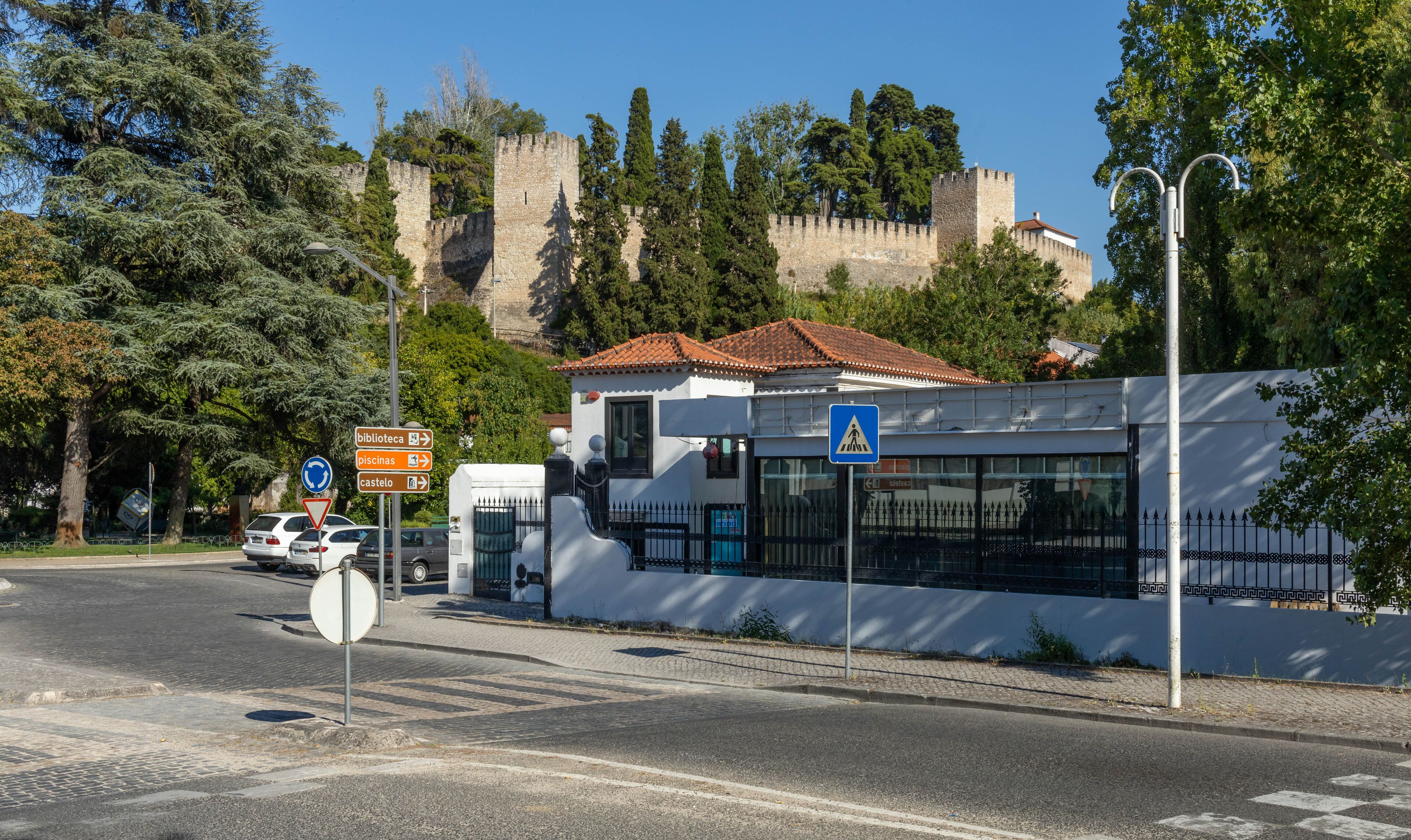 A street with a castle in the background, a white building with a red roof, and a pedestrian crossing sign.