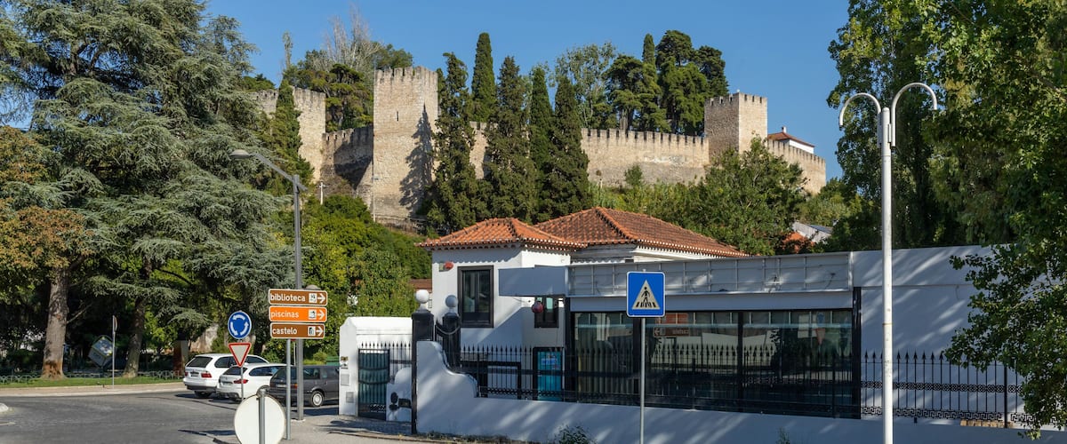 A street with a castle in the background, a white building with a red roof, and a pedestrian crossing sign.