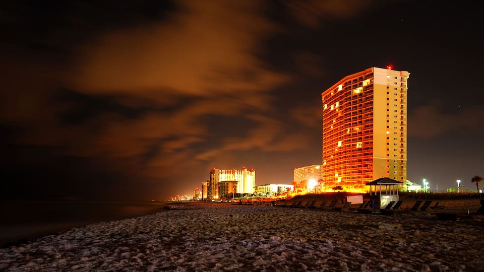 A beach with a large illuminated hotel and palm trees in the background.
