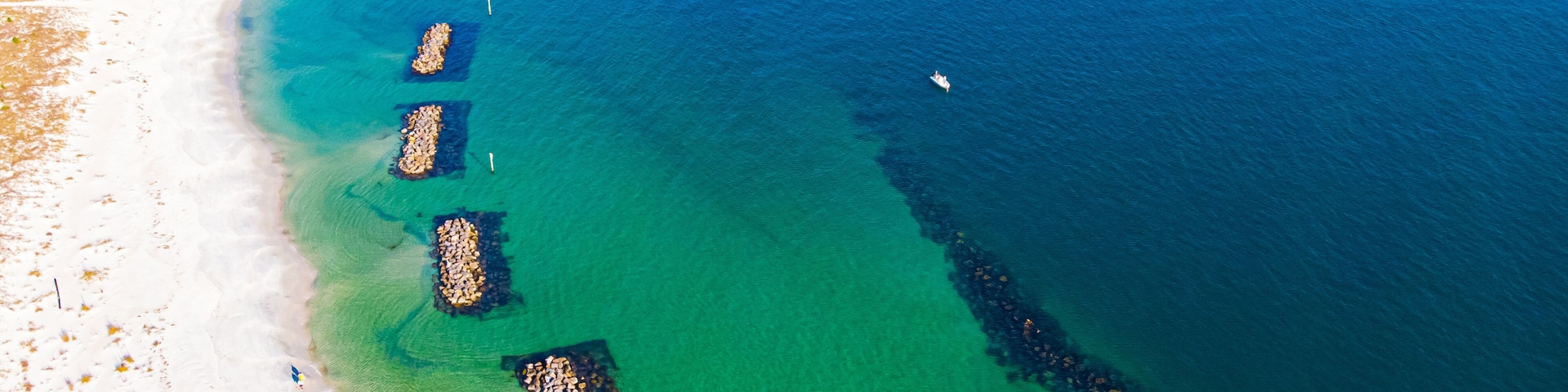 Un paisaje costero con aguas turquesas cristalinas, una playa arenosa y varios espigones que se adentran en el mar.