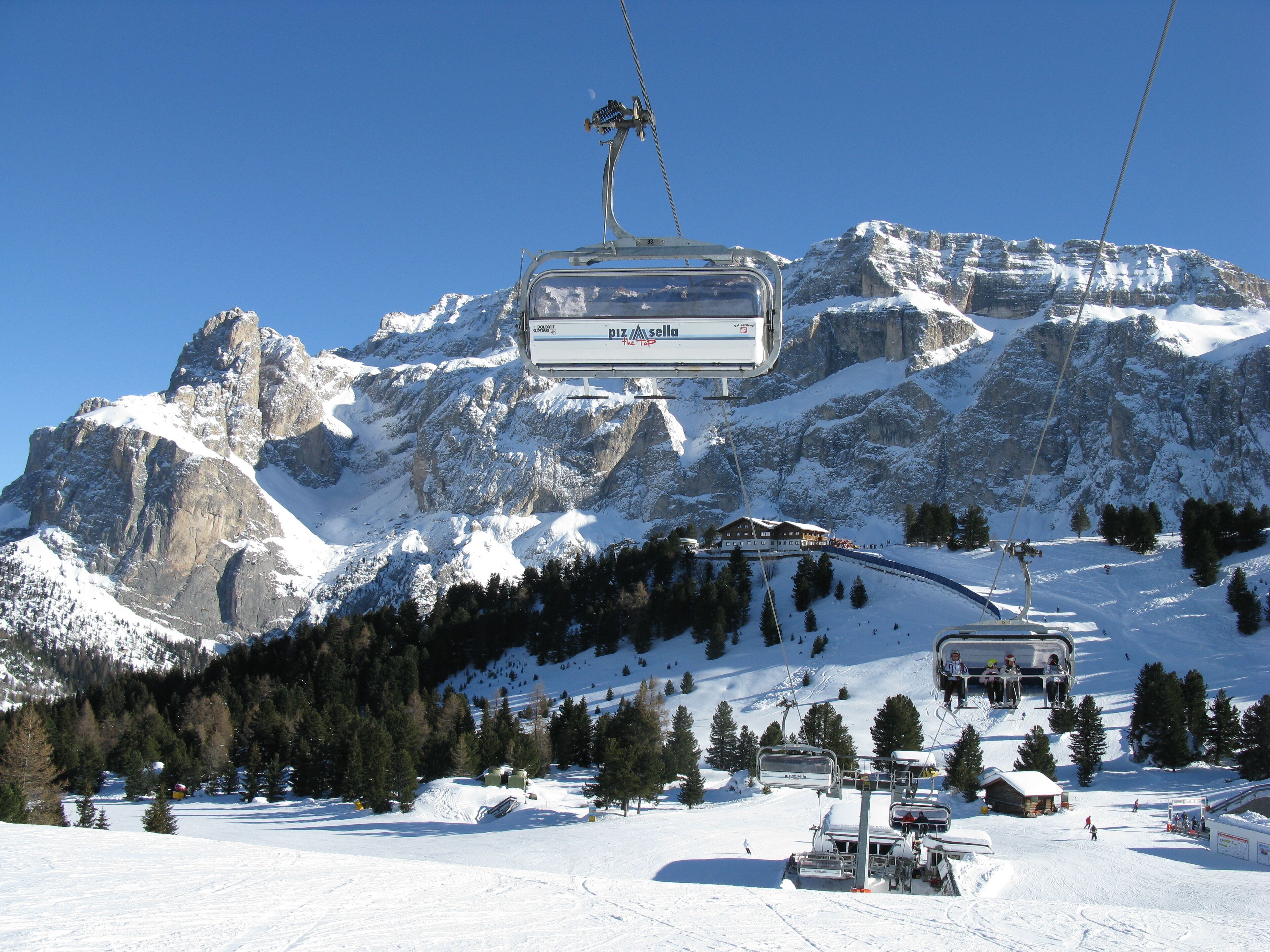 A ski lift with a mountain backdrop, snow-covered slopes, and a clear blue sky.