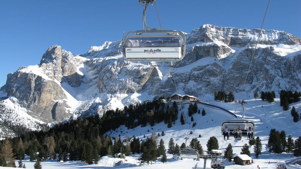 Un télésiège avec en toile de fond les montagnes, des pentes enneigées et un ciel bleu dégagé.