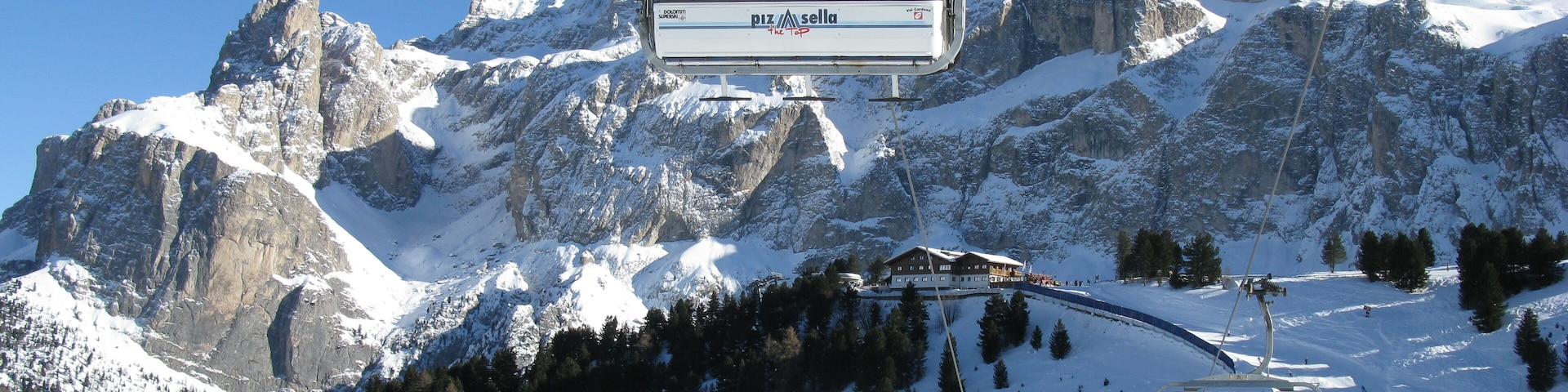 A ski lift with a mountain backdrop, snow-covered slopes, and a clear blue sky.