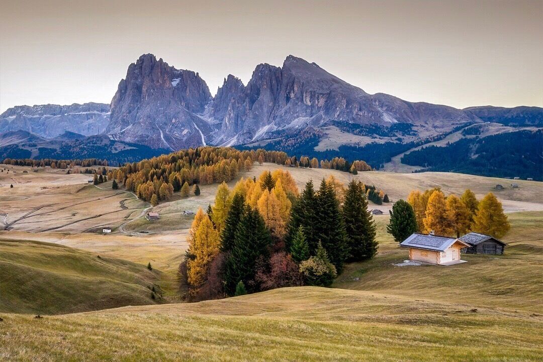 A mountainous landscape with autumn-colored trees and a small cabin.
