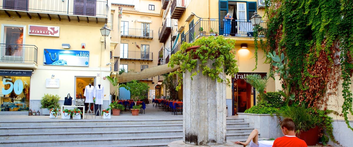 A fountain in a square with steps leading up to it, surrounded by buildings with shops and outdoor seating.