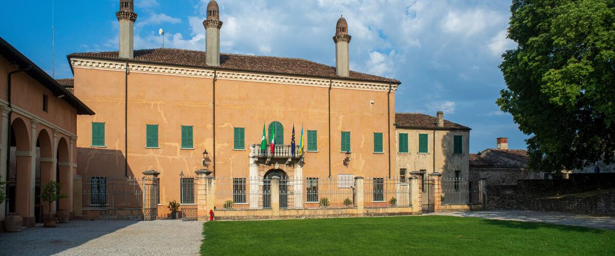 A historic building with a central balcony, green shutters, and multiple chimneys.