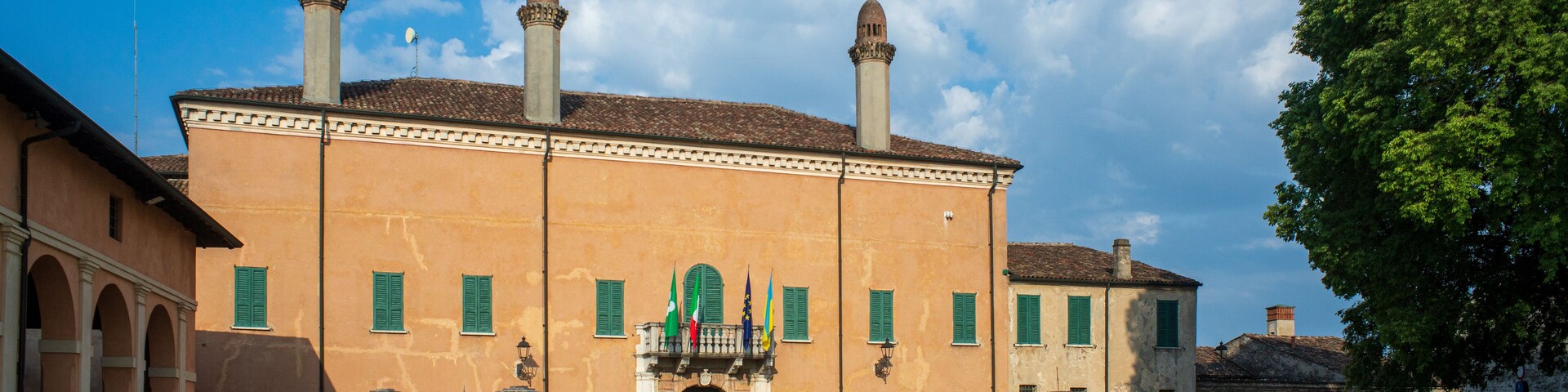 A historic building with a central balcony, green shutters, and multiple chimneys.