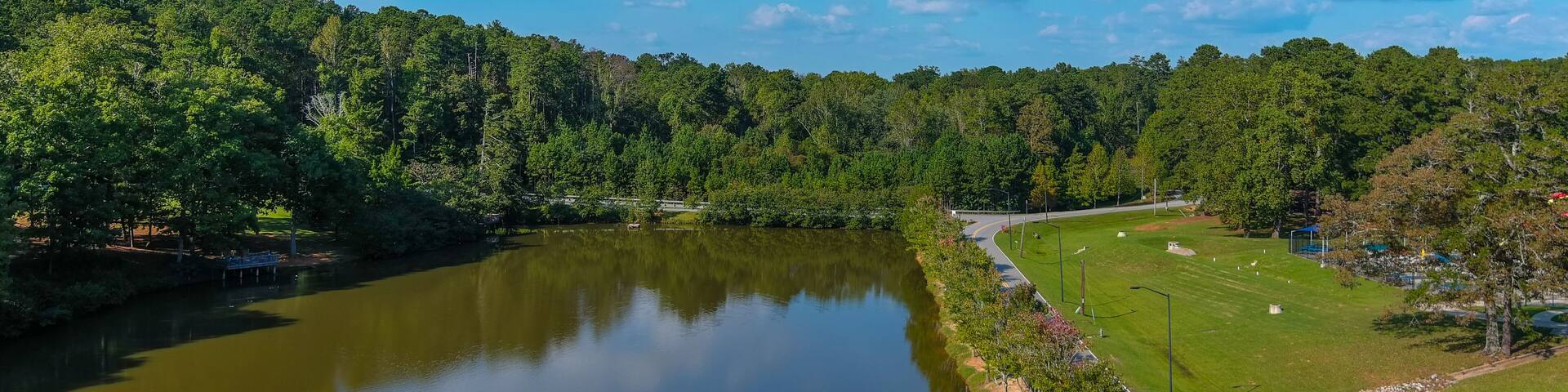 a gorgeous shot of the still green lake water surrounded by lush green and autumn colored trees with blue sky and clouds at Duncan Park in Fairburn Georgia USA