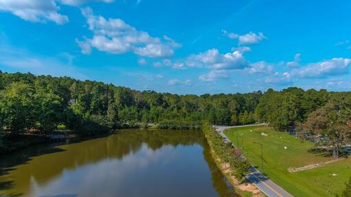 a gorgeous shot of the still green lake water surrounded by lush green and autumn colored trees with blue sky and clouds at Duncan Park in Fairburn Georgia USA