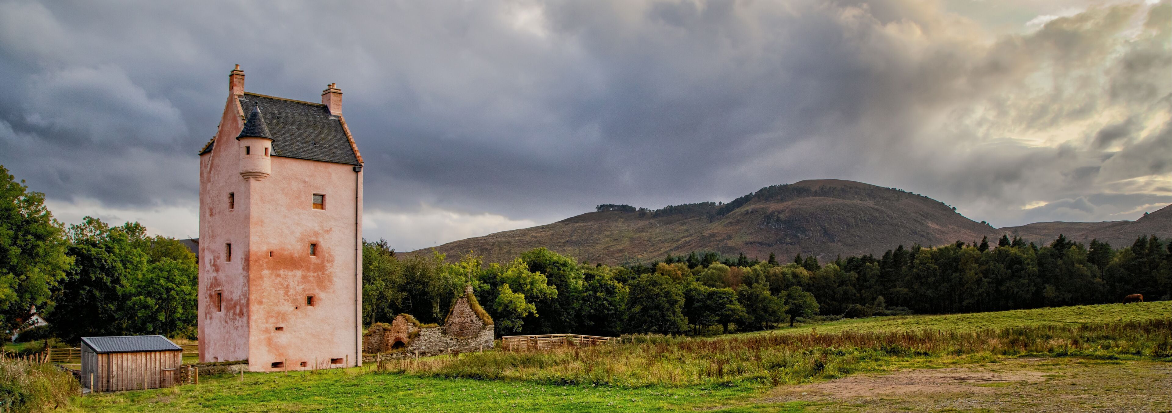 A pink tower, a stone house, and a forested hill.