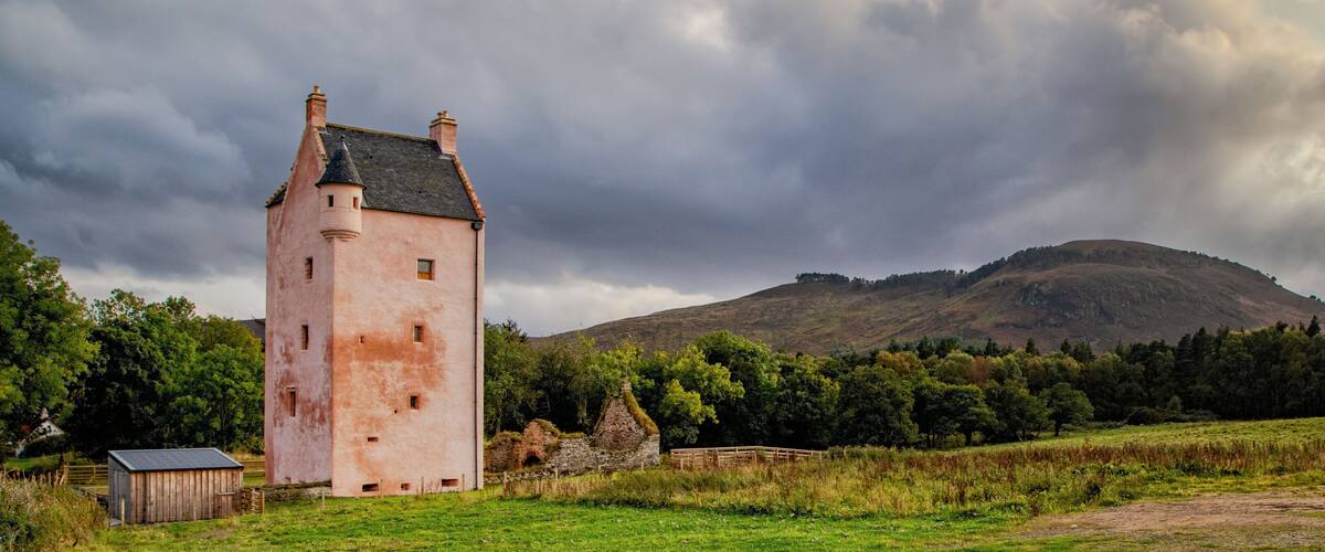A pink tower, a stone house, and a forested hill.