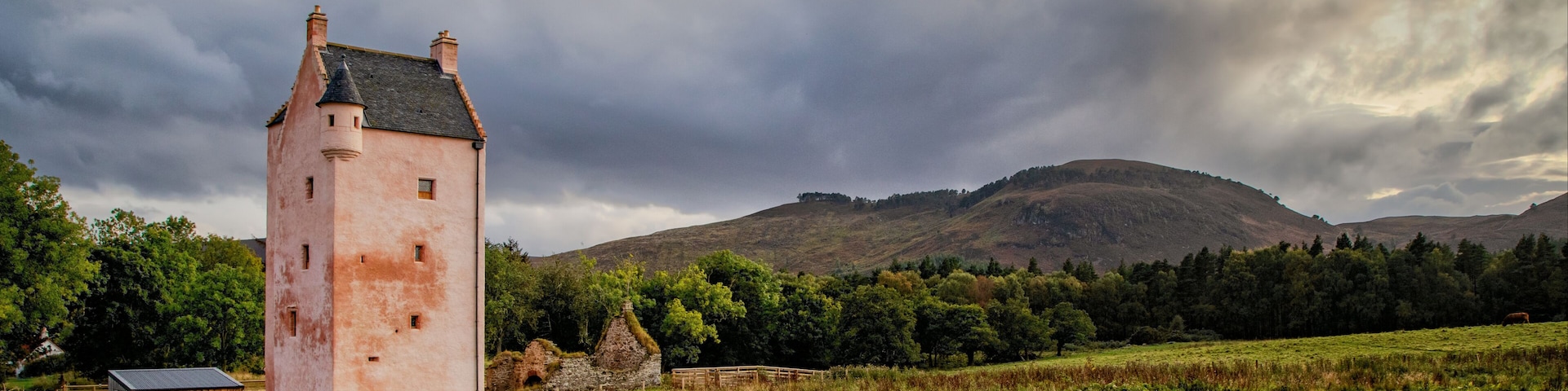 A pink tower, a stone house, and a forested hill.