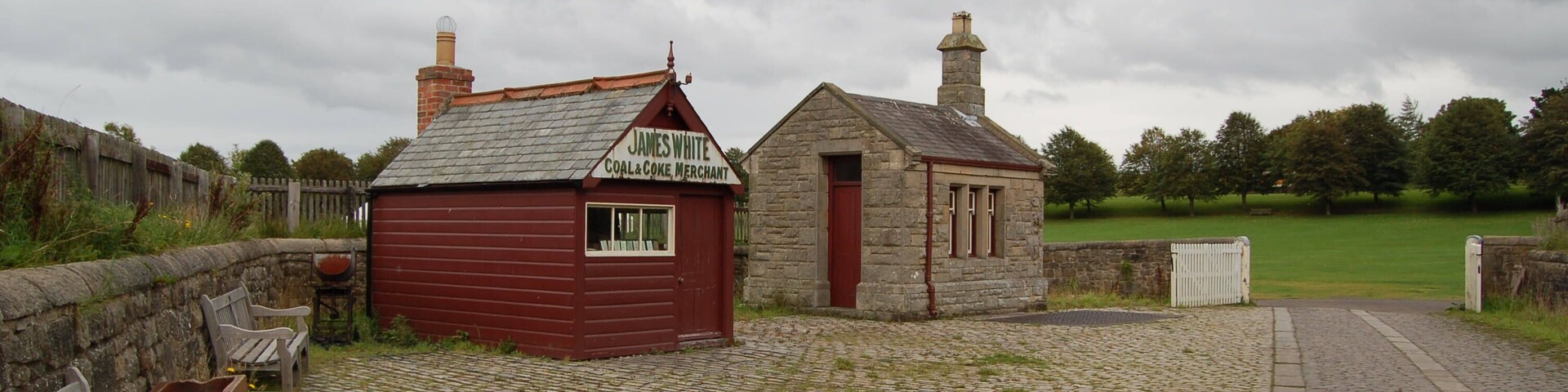 A stone building with a red door and a sign that reads "James White Coal Coke Merchant."