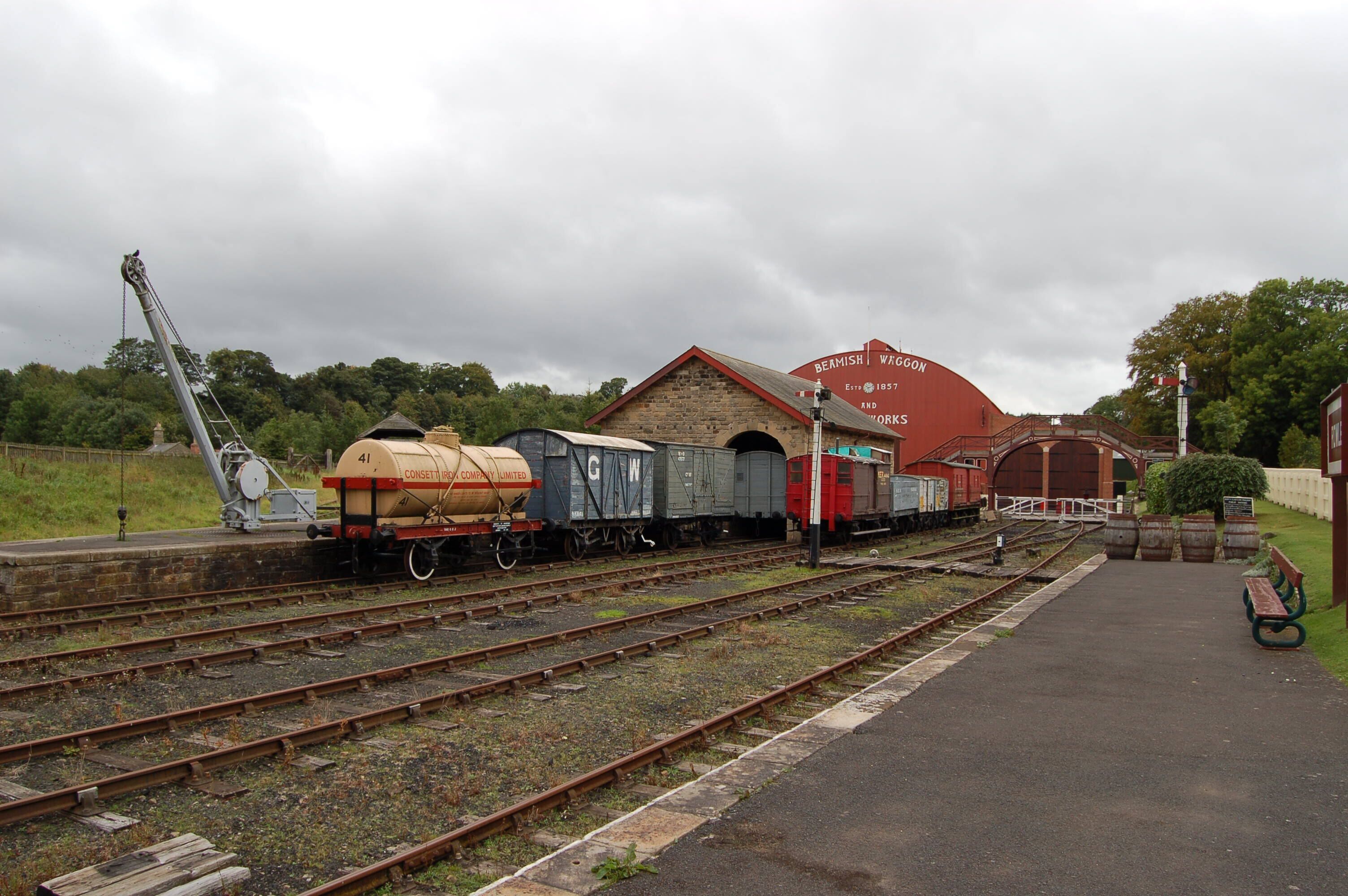 A railway station with multiple tracks, a red brick building labeled 'BERMISH WHOGON AND WORKS', and a crane.