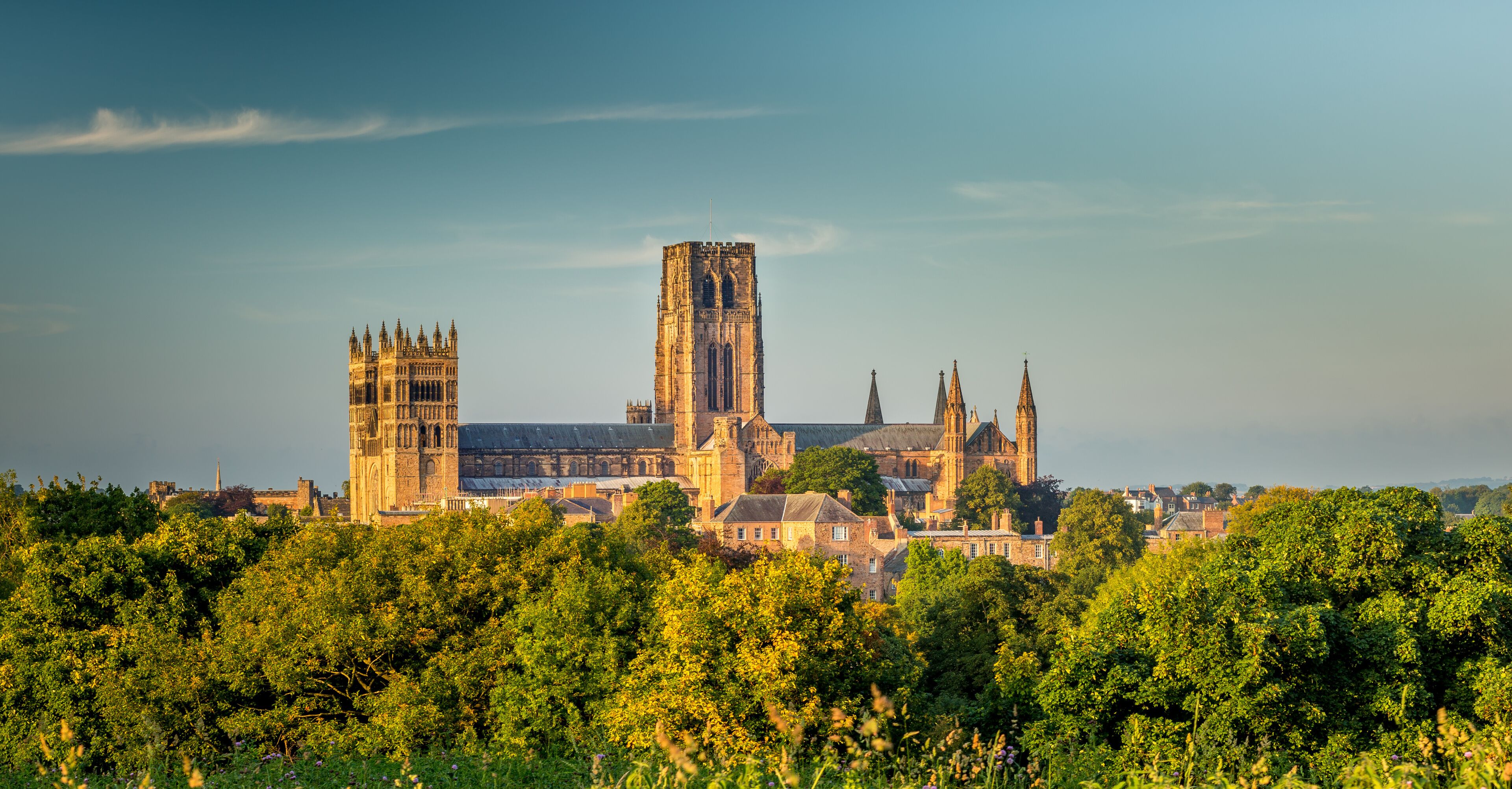 A historic cathedral with twin towers and a tall central spire, surrounded by lush greenery.