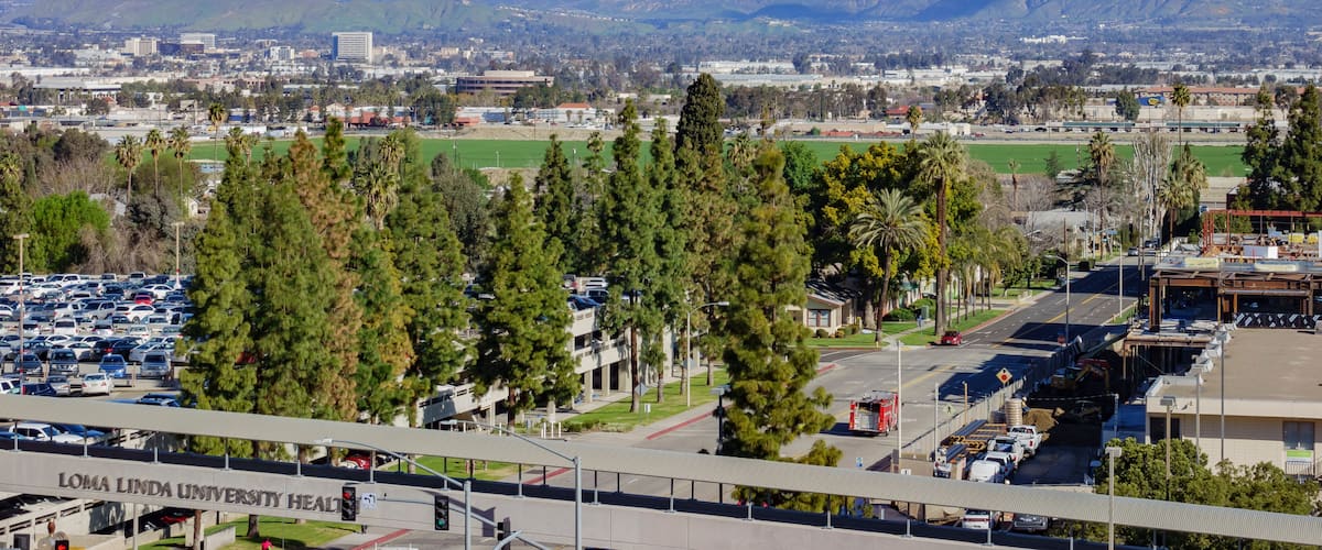 A university campus with parking lots, a sports field, and mountains in the background.