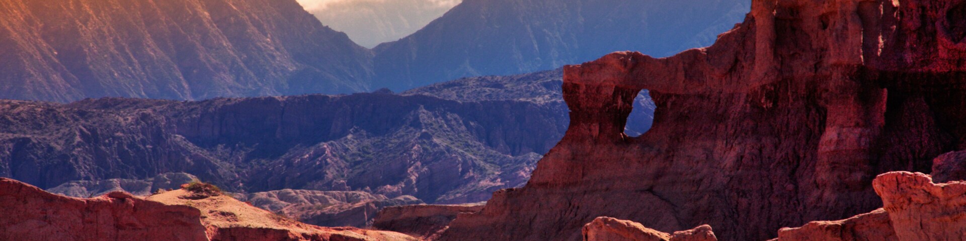 Un paisaje montañoso agreste con destacadas formaciones rocosas rojas y un valle.