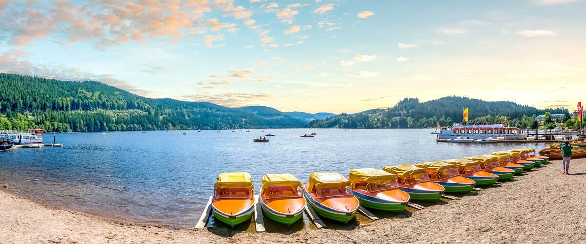 A lakeside with boats, a dock, and a forested mountain in the background.