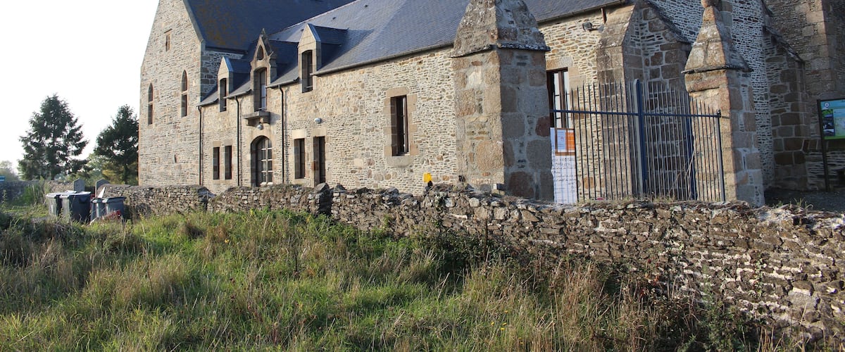 A stone building with a steep roof and a stone wall in front.