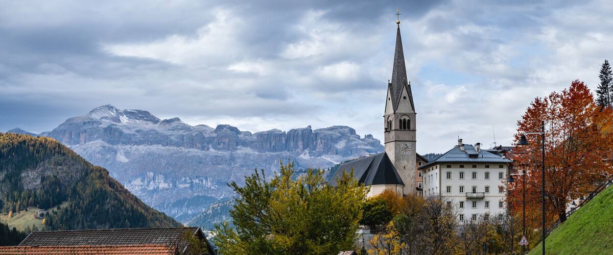 A church with a tall steeple, a mountain range, and autumn-colored trees.