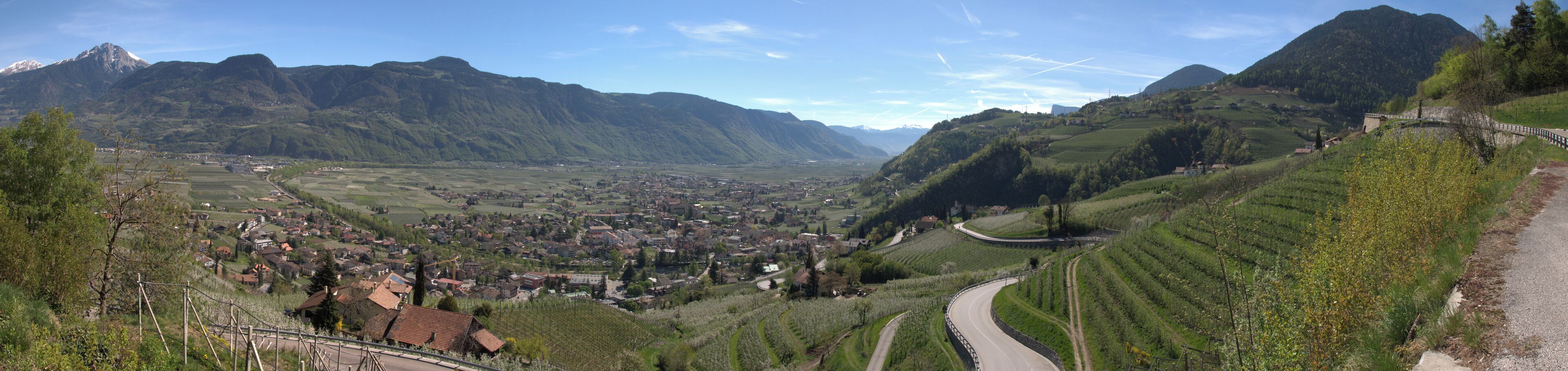 A valley with a town nestled between mountains, a winding road, and agricultural fields.
