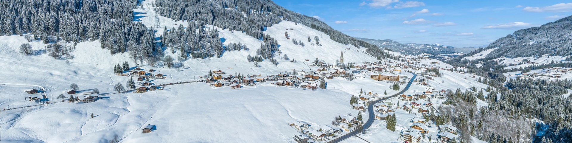A snow-covered mountain village with houses, a church, and a winding road.