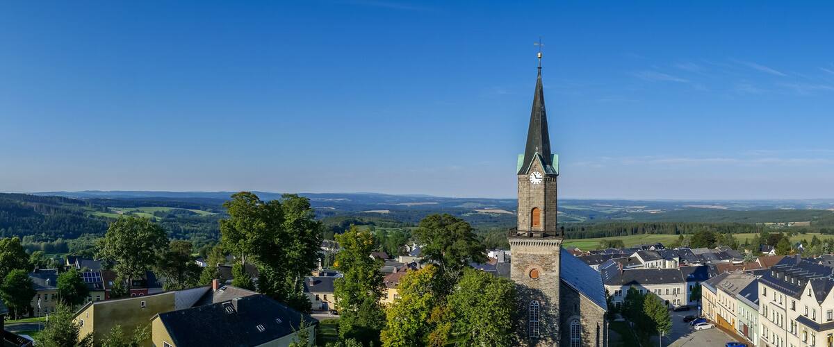 A town with a prominent church tower, surrounded by houses and lush green hills.