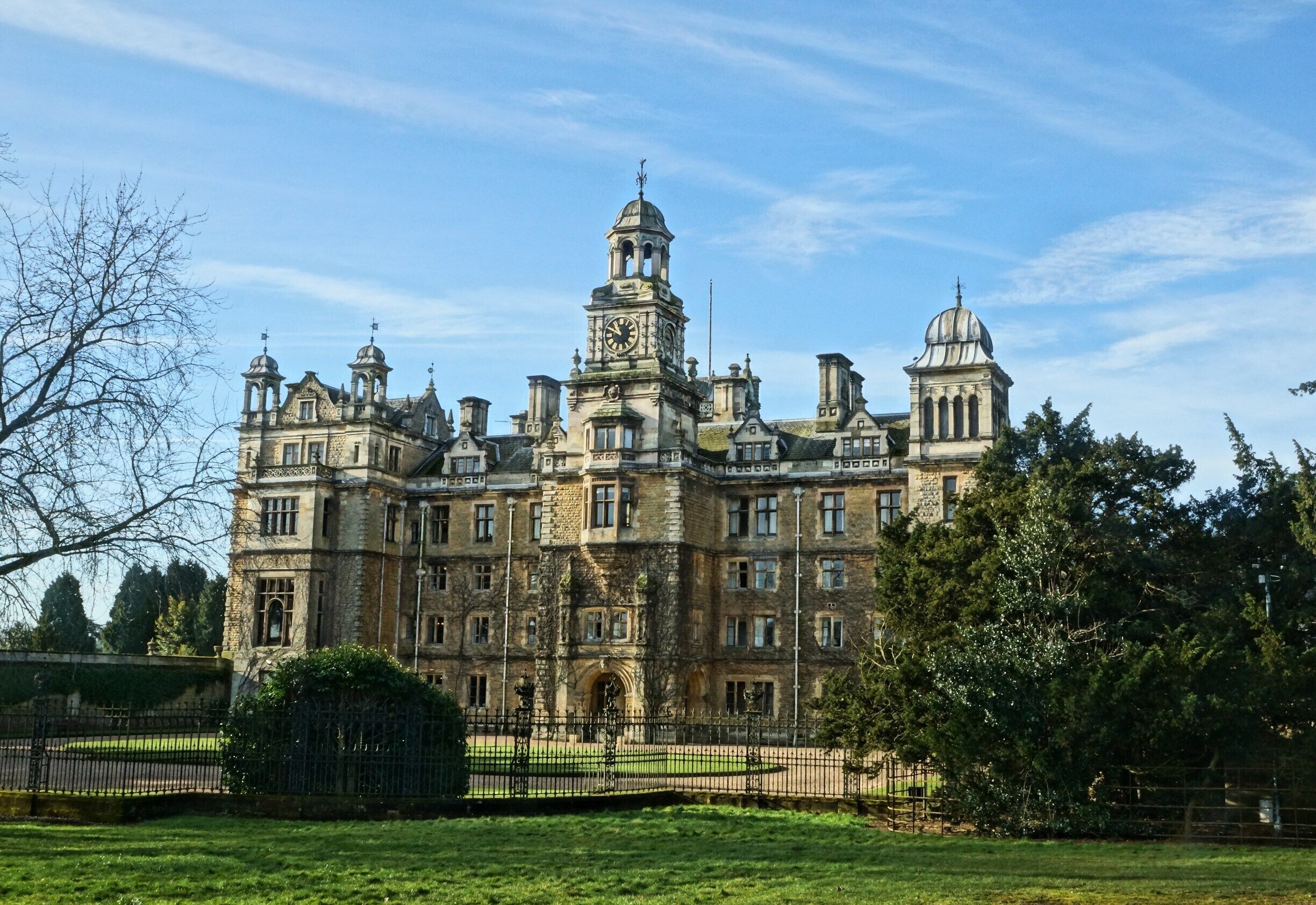 A large, historic building with multiple towers and domes, surrounded by a well-maintained lawn and trees.