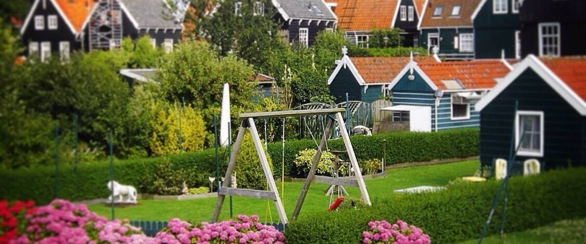 A garden with a swing set, pink flowers, and traditional houses with red roofs.