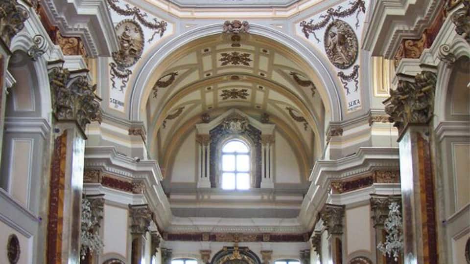 An ornate church interior with a high ceiling, detailed frescoes, and a central altar.