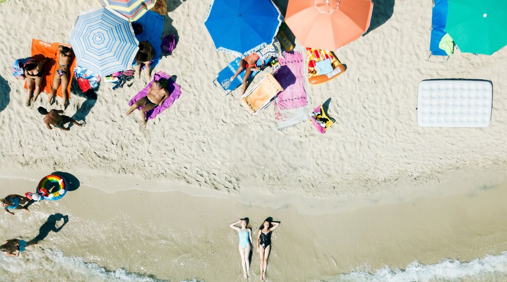 PUGLIA, ITALY - SEPTEMBER 06, 2018: Aerial view two young girls in swimwear lie on sand beach Punta Prosciutto Italian Maldives. Summer vacation. People sun bathe swim relax under umbrellas. Sea waves