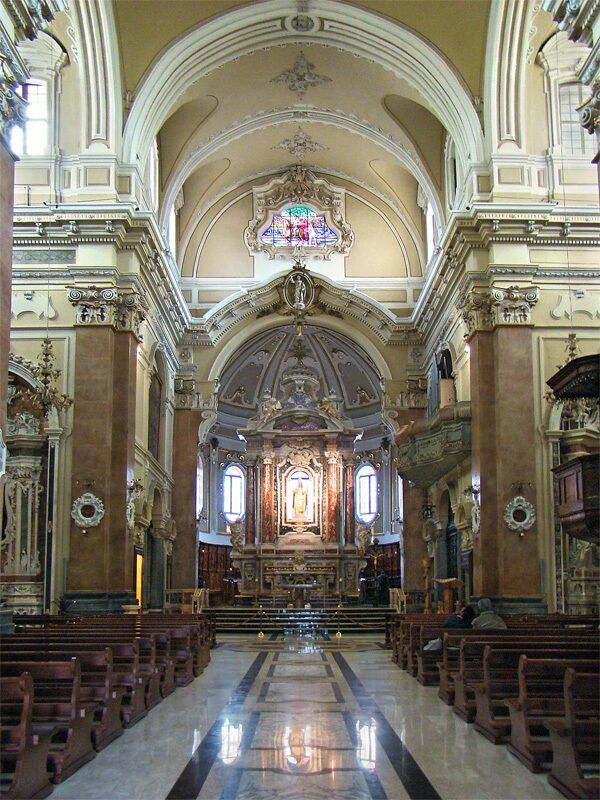 An ornate church interior with a central altar, pews, and stained glass windows.