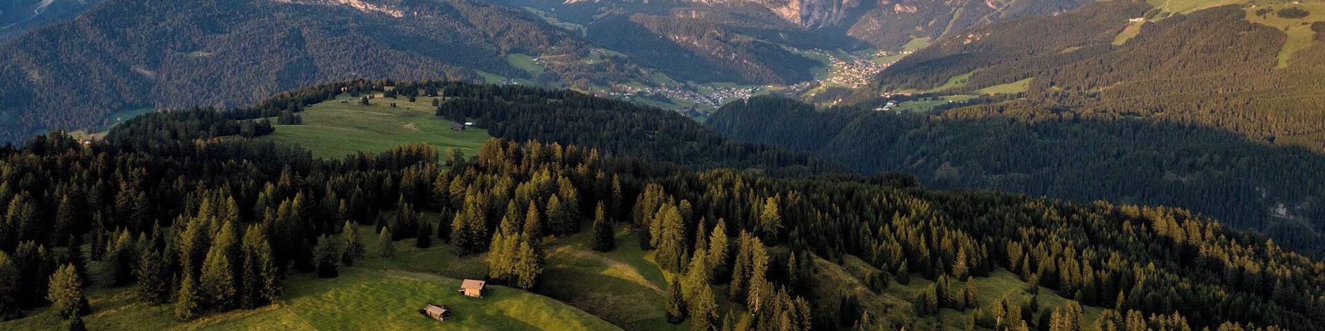 A mountainous landscape with a valley, forested areas, and a small building.