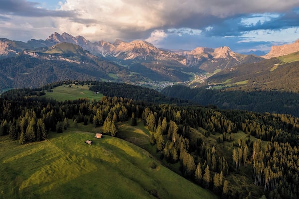 Un paysage montagneux comprenant une vallée, des zones boisées et un petit bâtiment.